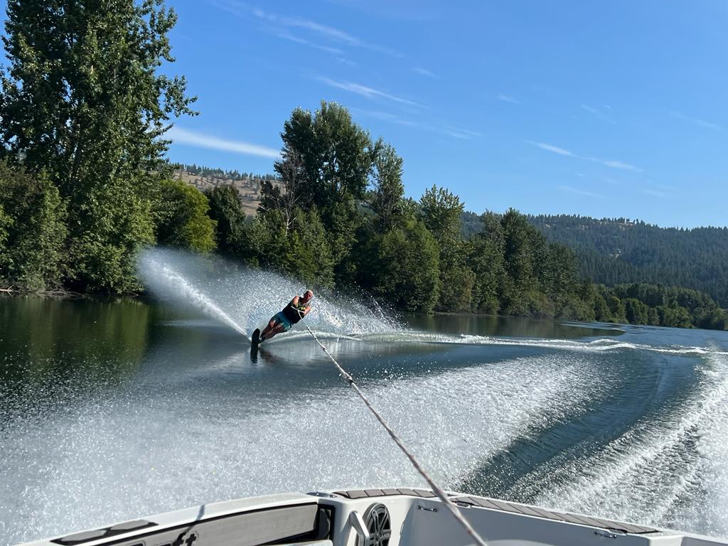 A skier carving hard, throwing a large spray of water, seen from the boat