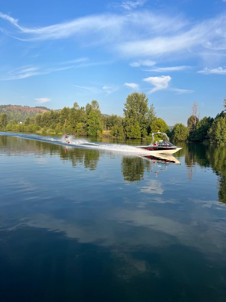 A skier behind a boat on a calm lake under a partly clouded sky